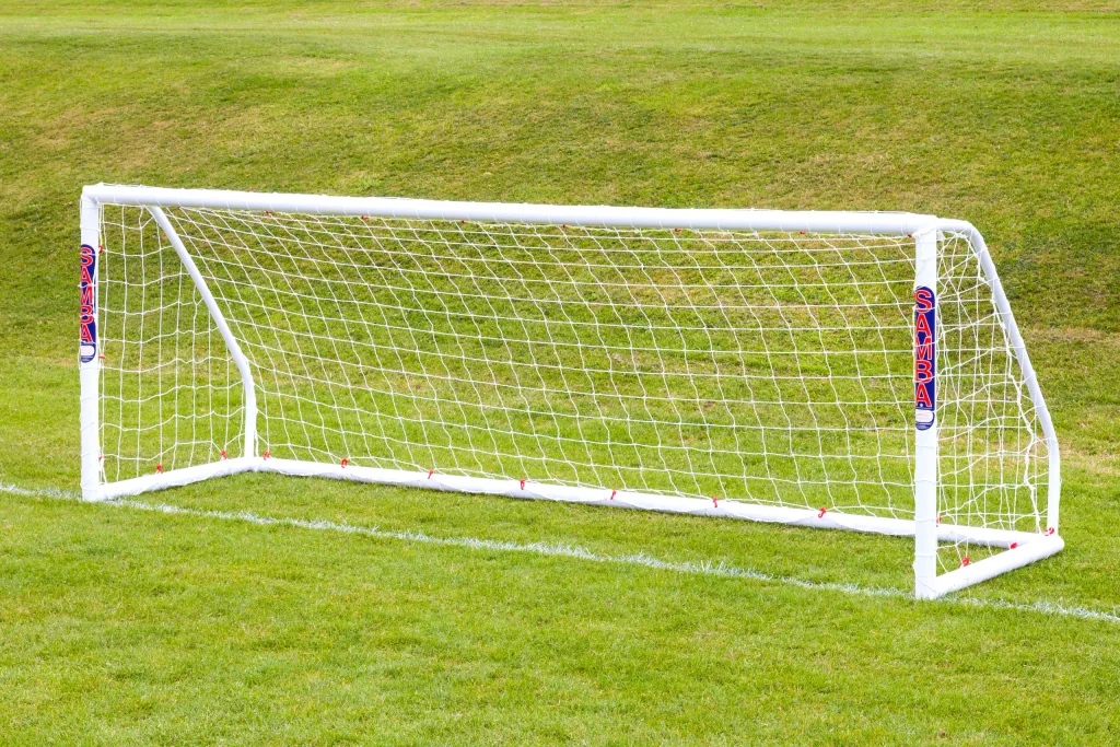 White freestanding soccer goal with net on grass and SAMBA stickers on the posts.
