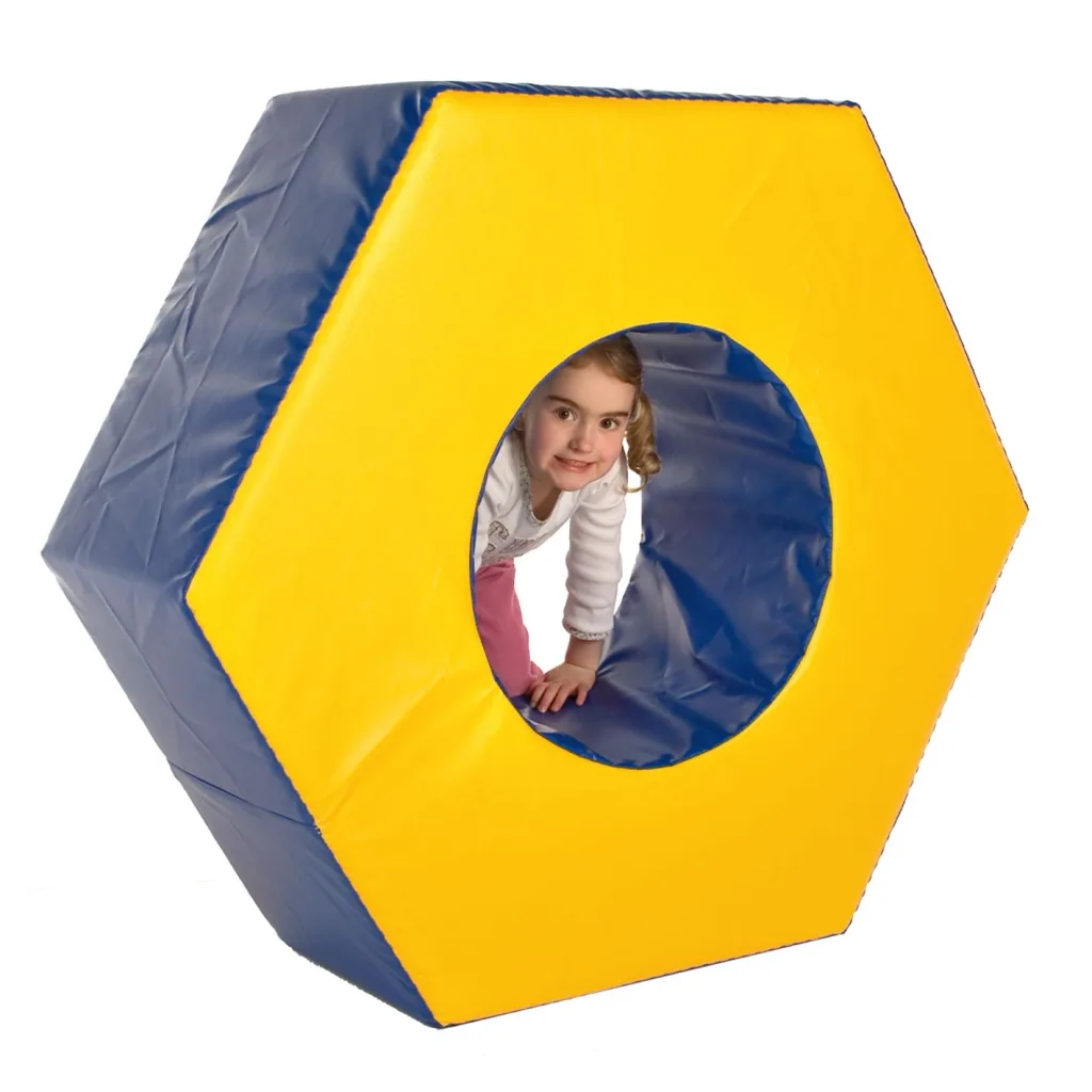 Young girl crawling through a yellow hexagonal foam play tunnel with a blue interior, smiling at the camera.