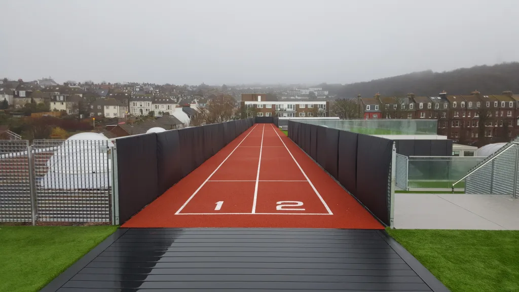 Rooftop red two-lane running track with white lane lines numbered 1 and 2, flanked by dark padded wall panels made of smooth polyester PVC.