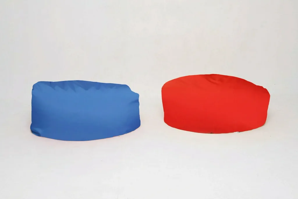 Two child polyester pie bean bags, one blue and one red, resting on a plain white background.