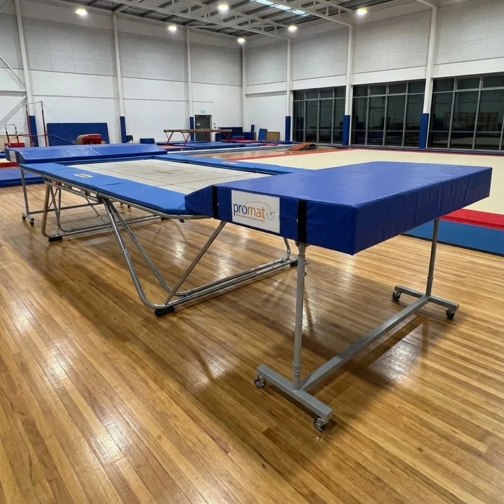 Blue spotting end decks labeled promat on wheeled metal frames beside a trampoline in a gym.