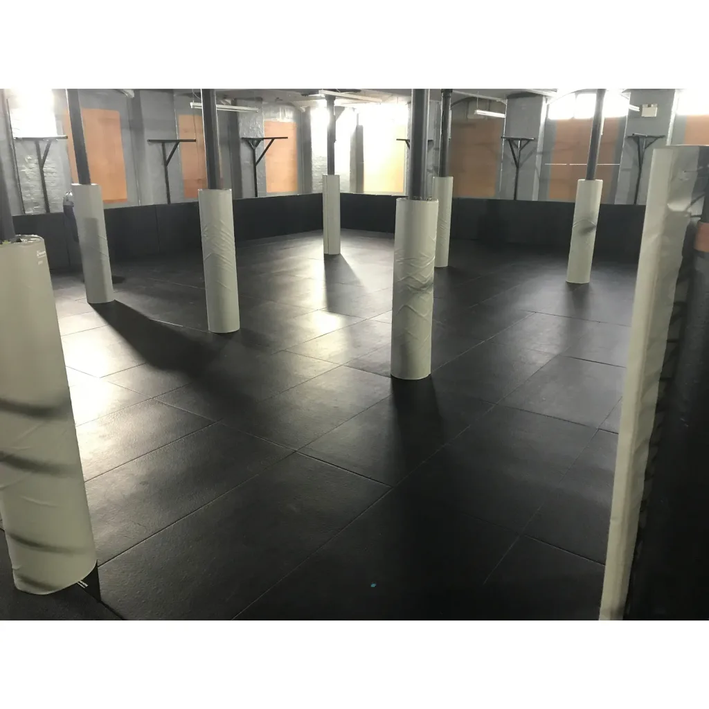 Several white round post pads covering metal columns on a black tiled mat floor inside a spacious industrial-style training room.