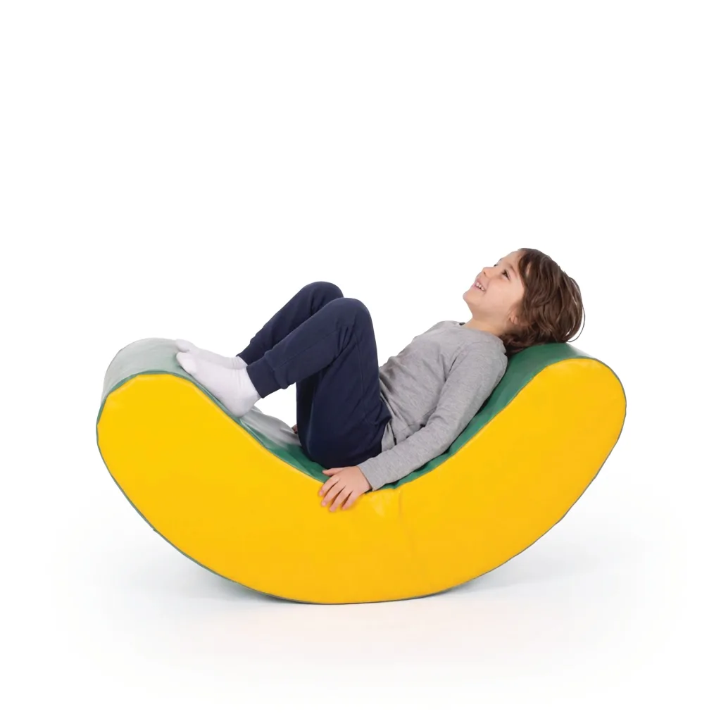Child lying back and smiling on a yellow and green curved foam rocker with knees bent and white socks.
