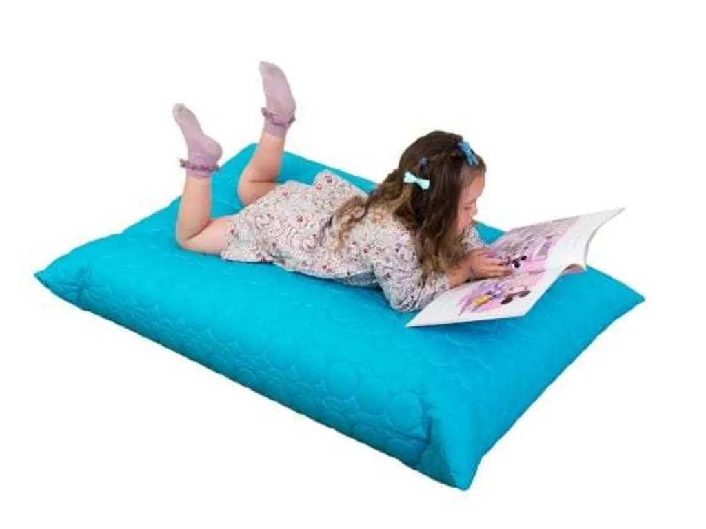 Child lying on her stomach reading a book on an aqua padded giant floor cushion.