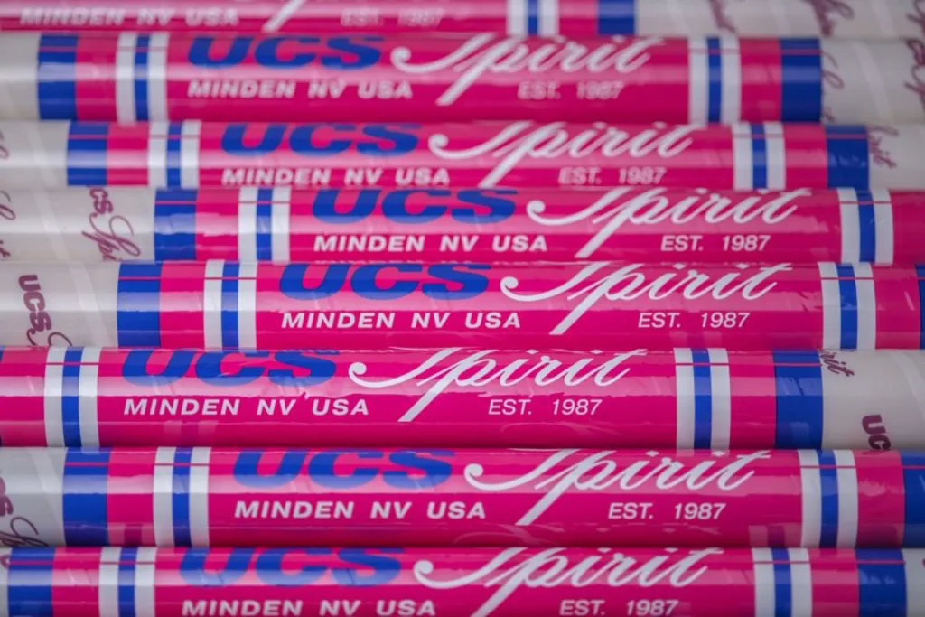 Stacked pink and white vaulting poles with blue stripes labeled "UCS spirit MINDEN NV USA EST. 1987".