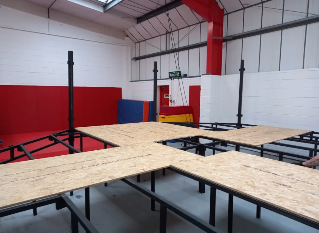 Platform training cage with steel powder-coated frame and raised deck panels inside a gym, digital clock reading 17:42:39.