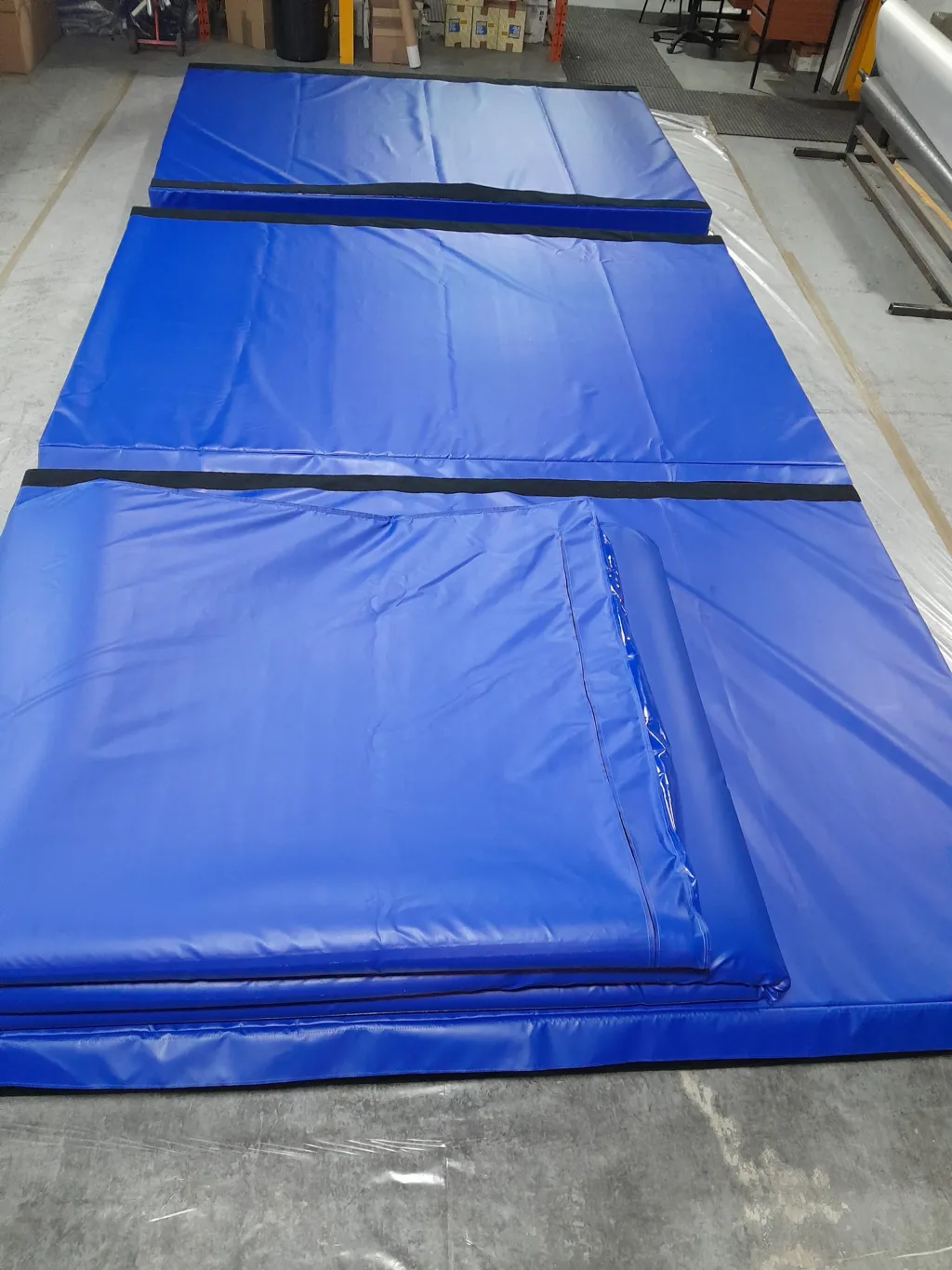 Three large blue gymnastics landing mats joined by black hook-and-loop strips laid flat in a warehouse space.