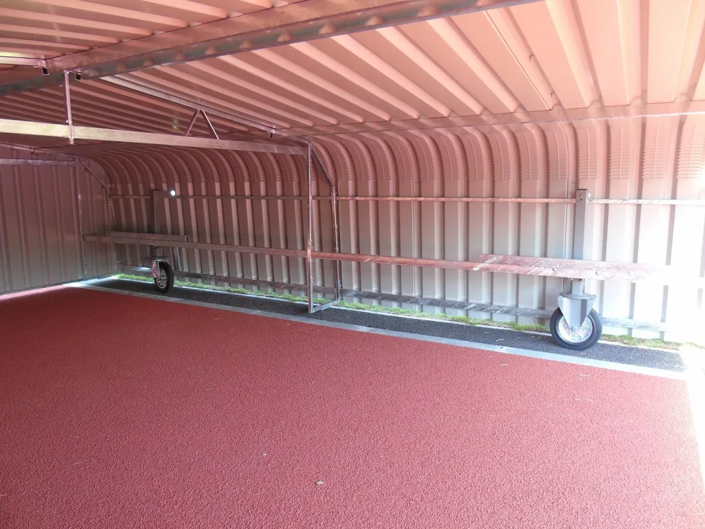 High jump wheel-away covers with galvanised welded steel frame and epoxy-coated steel cladding on caster wheels under a metal shelter above red track.