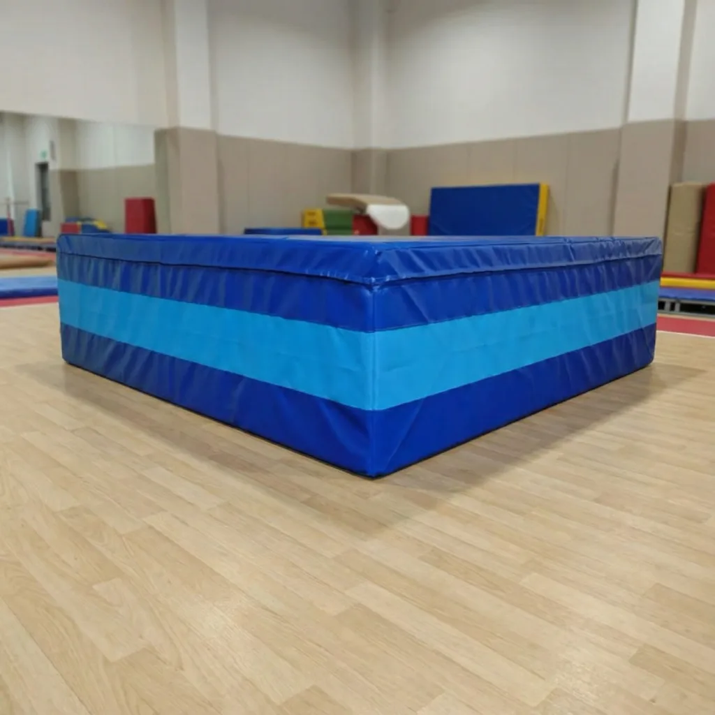 Blue soft-landing pit with a lighter blue horizontal stripe resting on a gymnasium floor.