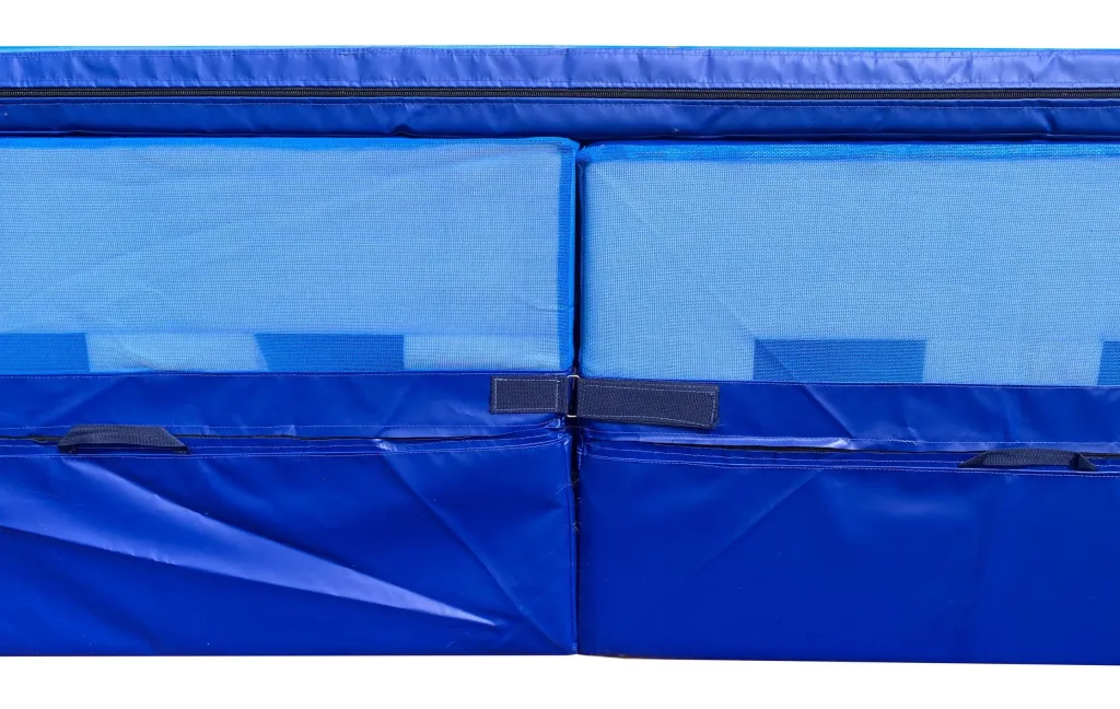 Close-up of a blue gymnastics landing pit front seam showing mesh-sided top mats with a blue PVC cover and Velcro straps.