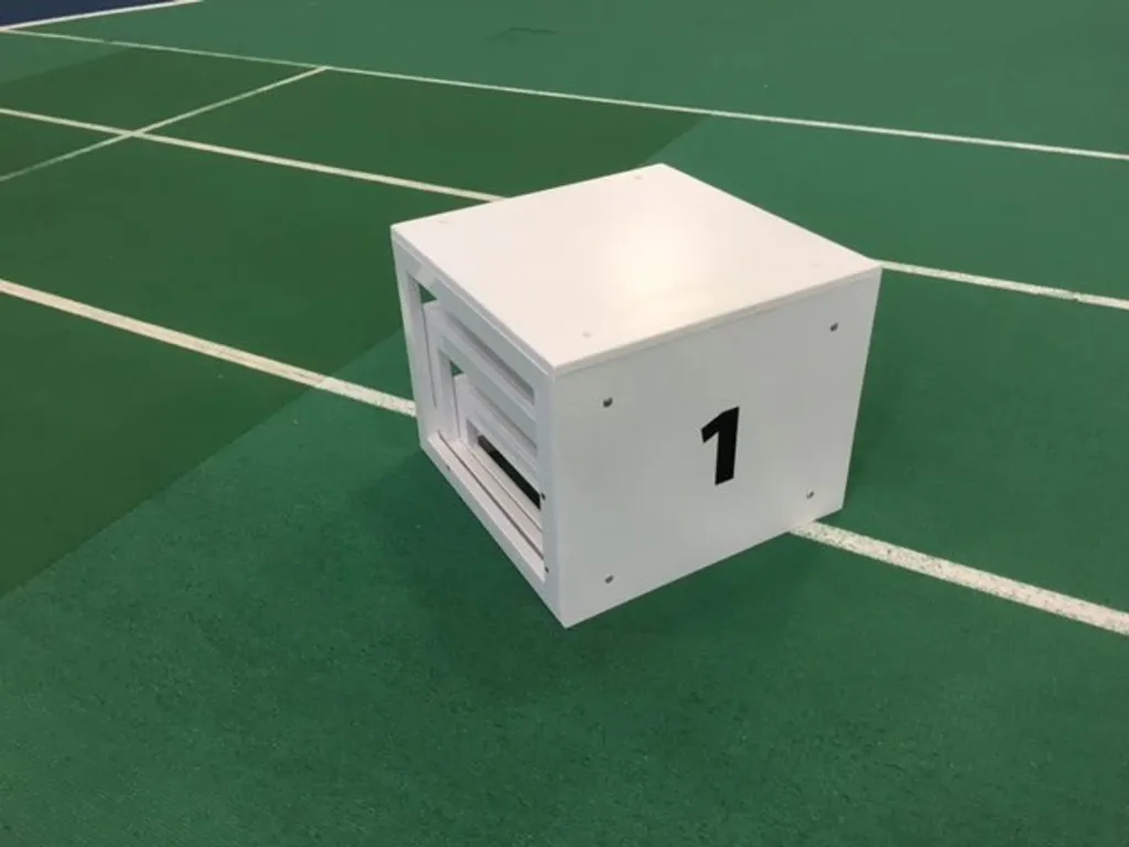 White winners podium with black 1 on the front, placed on a green indoor sports court with white lines.