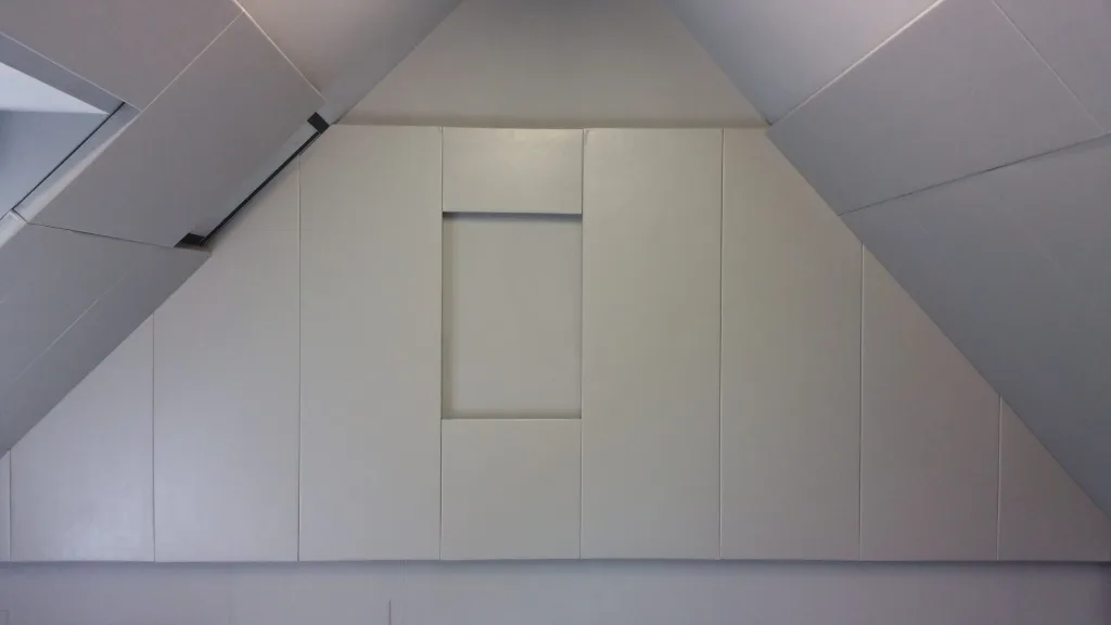Light gray padded panels cover a pitched attic wall, forming a recessed rectangular alcove at center.