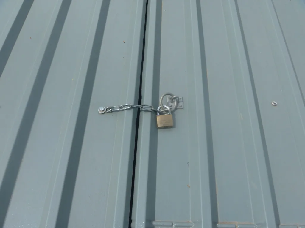 Two adjacent steel, epoxy-painted cover panels joined at a seam and secured by a short chain through eyelets with a padlock.