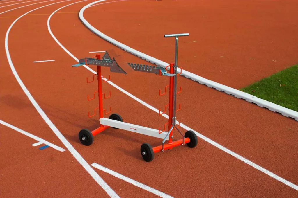 Starting block rack with stainless steel tubes, four wheels and multiple hooks for up to ten blocks, positioned on a red running track.
