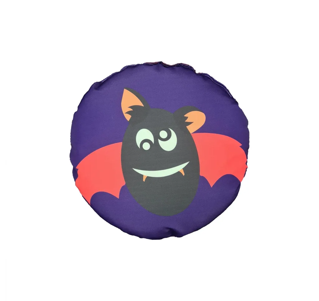 Round purple cushion with a smiling cartoon black bat face, red wings, orange ears and pale green eyes and fangs.