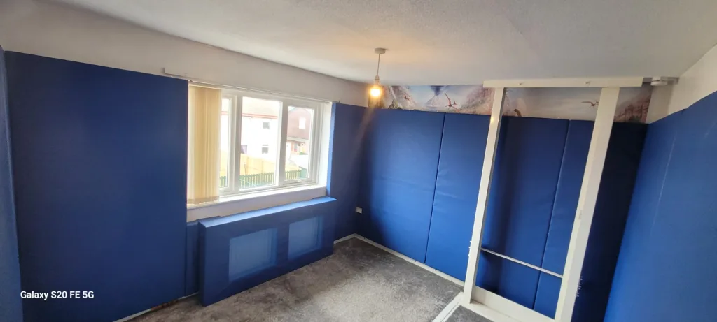 Blue padded walls and a padded radiator cover in a small room with a window and hanging light, with the text Galaxy S20 FE 5G in the corner.