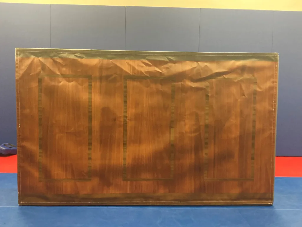 Large rectangular foam module with brown woodgrain print and three rectangular panel outlines, placed on blue mats in front of a blue wall with a yellow strip.