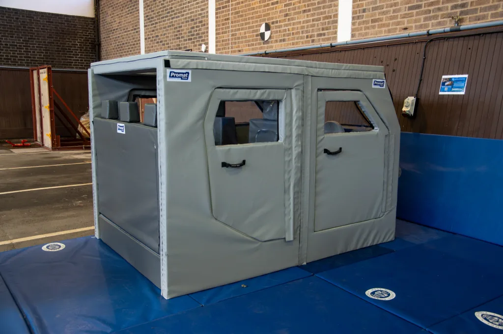 Grey padded training car with heavy-duty PVC cover and foam, window cutouts and black handles, placed on blue mats.
