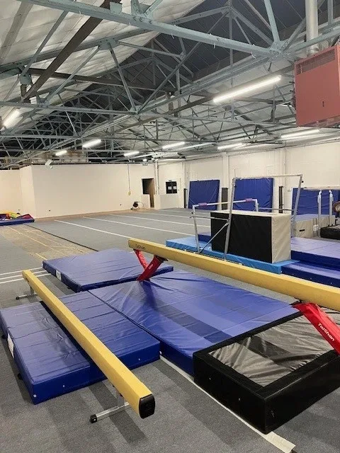Two yellow low balance beams with red supports resting on blue crash mats in a spacious gymnastics hall.