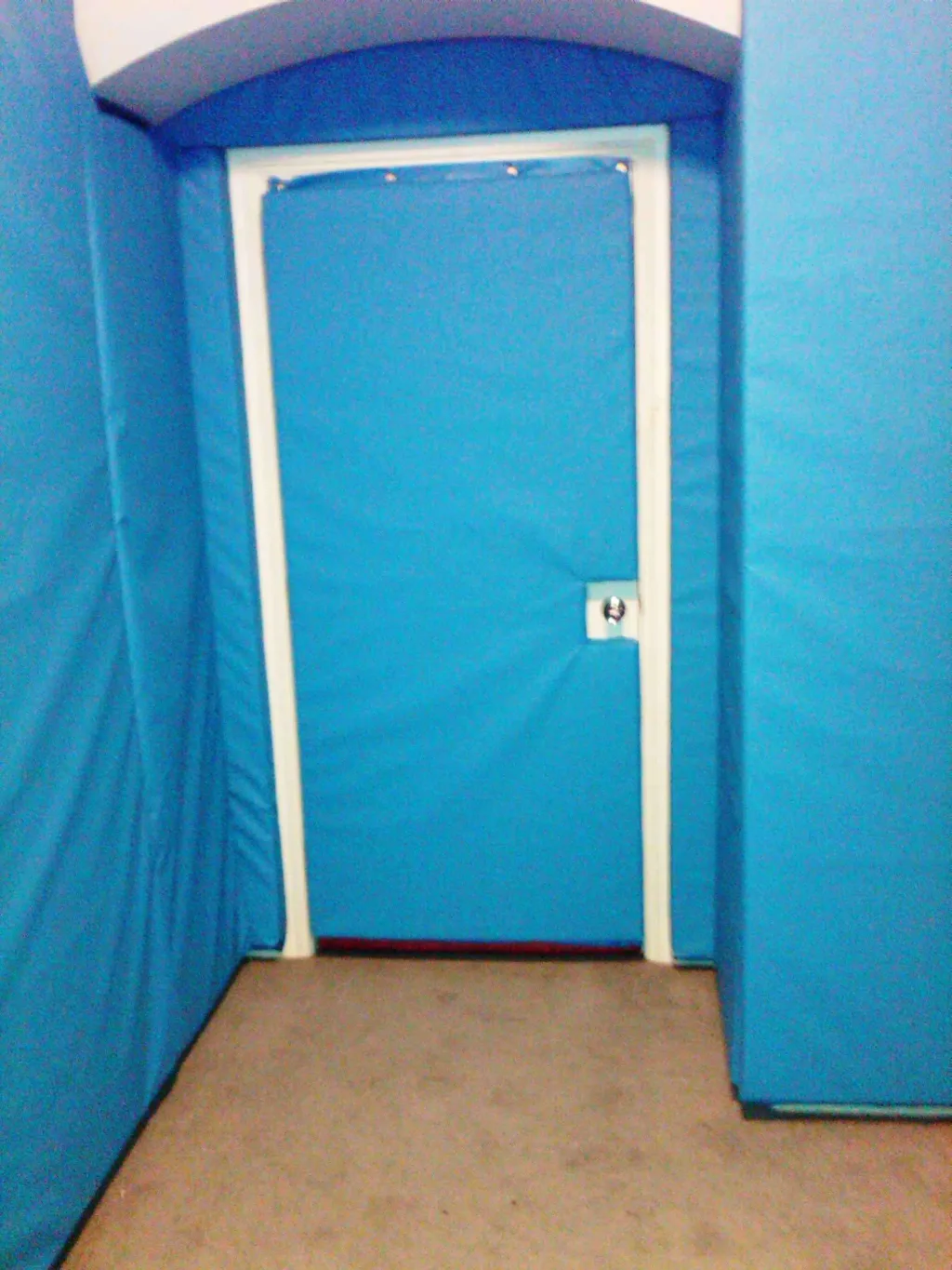 Padded blue door and surrounding blue padded walls in a small control and restraint room with beige carpet and a flush metal handle.