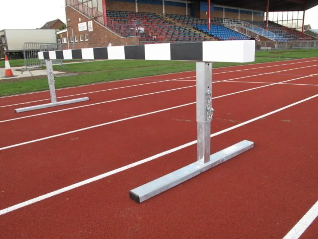 Steeplechase barrier with laminate-finished solid wood black-and-white top and galvanised steel legs positioned on a red running track.