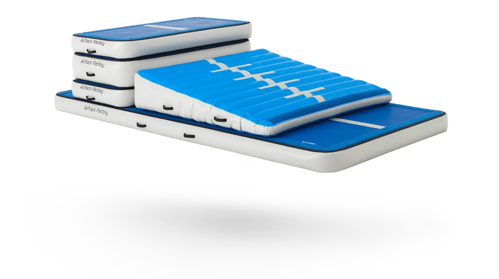 Blue and white inflatable gymnastics mats stacked with a sloped incline on top, handles visible and text "AirTrack Factory".