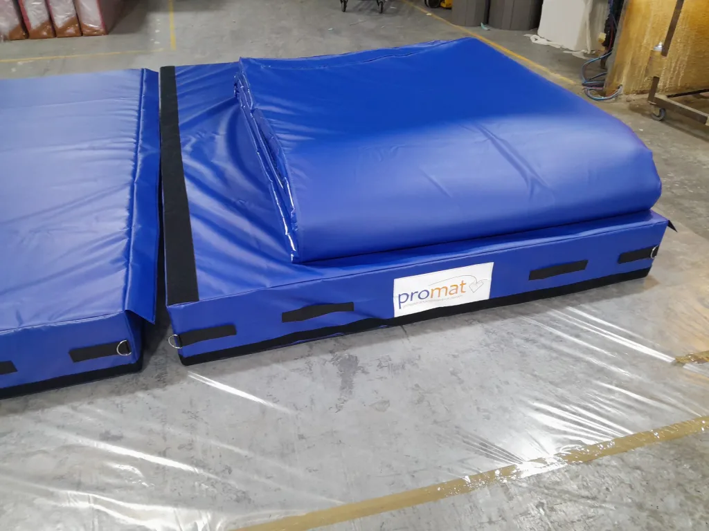 Blue padded landing area made of three connected modules with a folded top mat, black hook-and-loop strips, and a label reading promat.