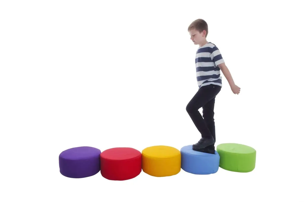 Boy stepping across five round cotton-covered foam seating pods in a row, colored purple, red, yellow, blue and green.