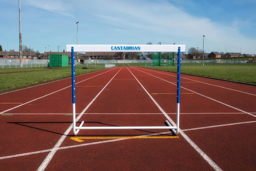 White training hurdle with CANTABRIAN on the top board, standing on a red outdoor running track.