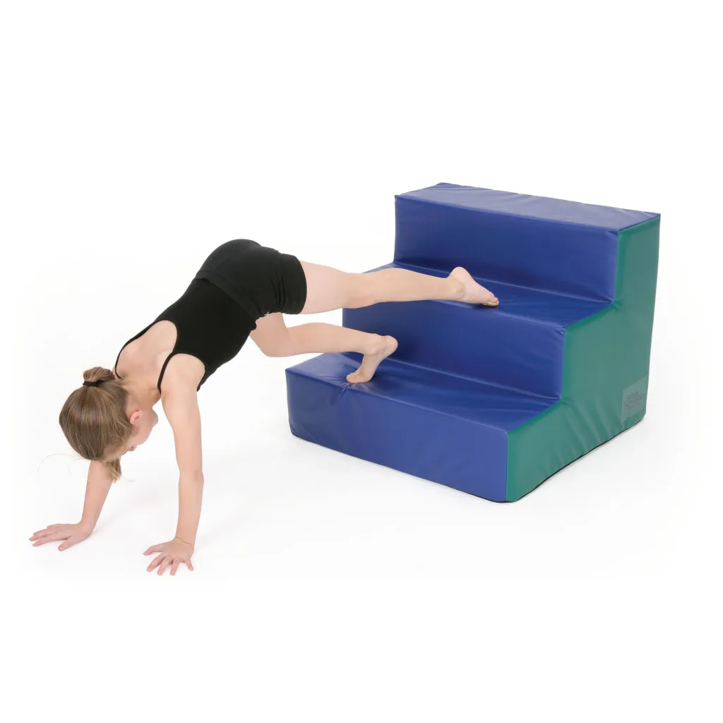 Child in a black leotard with hands on the floor climbing blue and green foam step blocks.