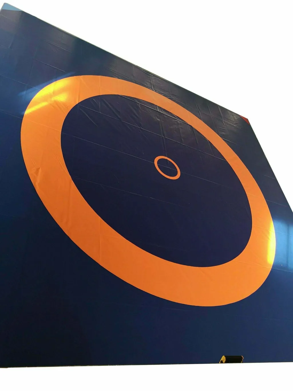 Large dark blue wrestling mat with an orange circular fight zone and a small orange inner circle on a vinyl cover.