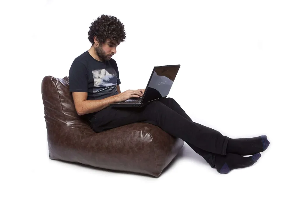 Brown faux leather teen/adult bean chair with a supportive backrest, shown with a seated person using a laptop.
