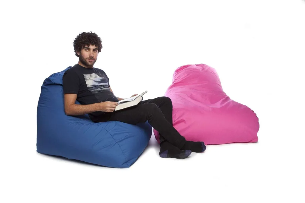 Man sitting on a sky blue bean chair reading a book with a pink bean chair beside him.