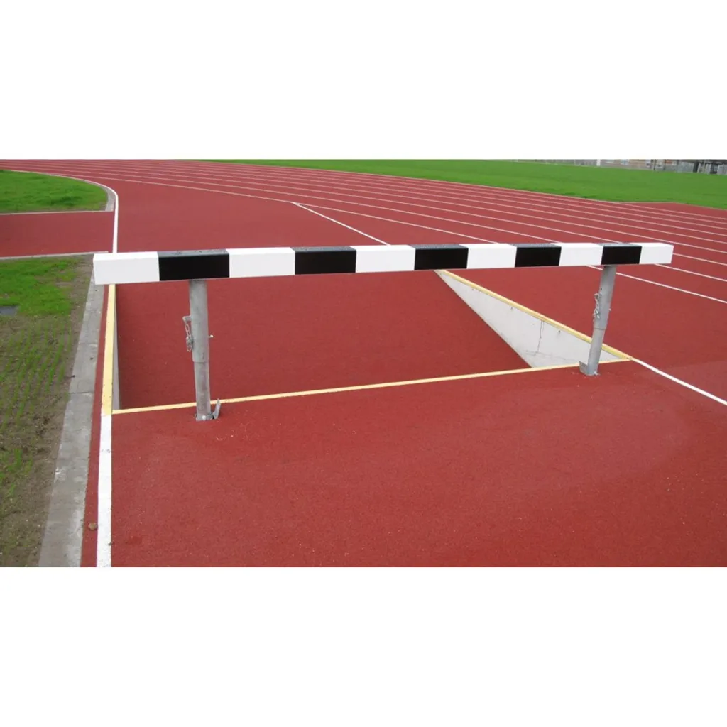 Water jump barrier spanning a water pit on a red running track, with galvanised metal uprights and a black-and-white wooden bar.