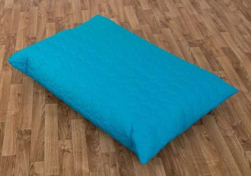 Large padded child floor cushion in aqua with quilted circular stitching resting on a wooden floor.