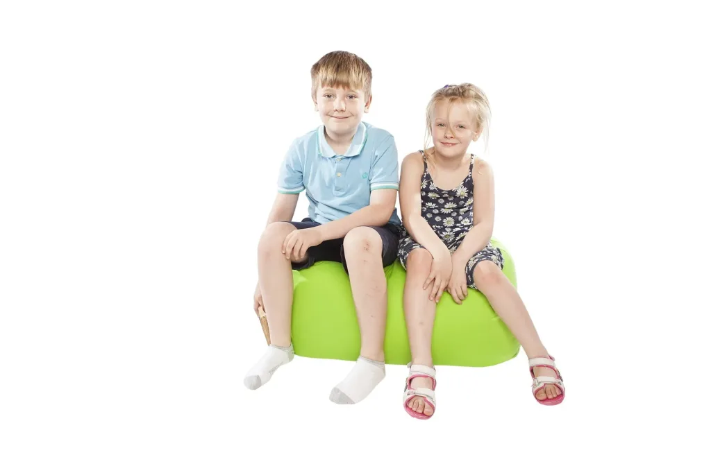 Two children sit on a lime green polyester child bean bench, smiling with one holding a small book.