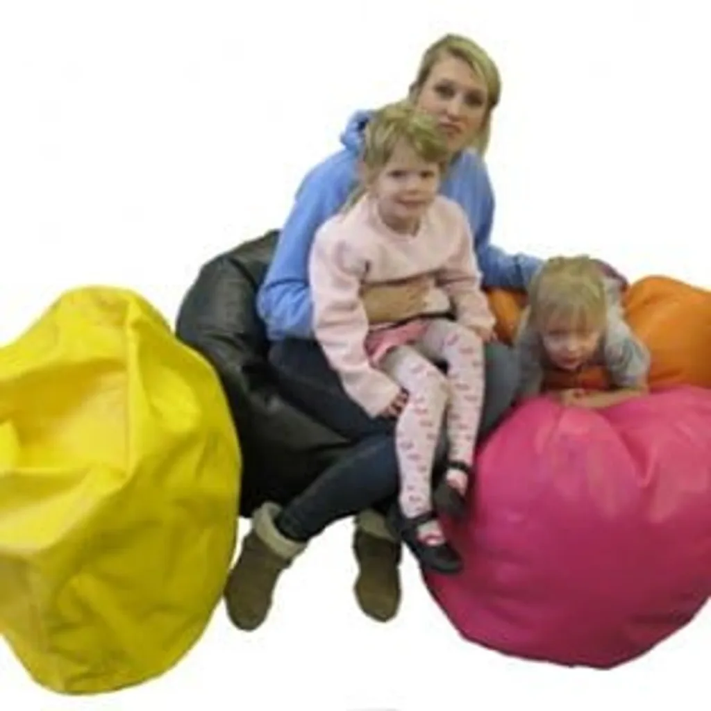 Woman holding a child seated on a black faux leather bean bag, another child leaning on a pink one with a yellow bean bag beside them.