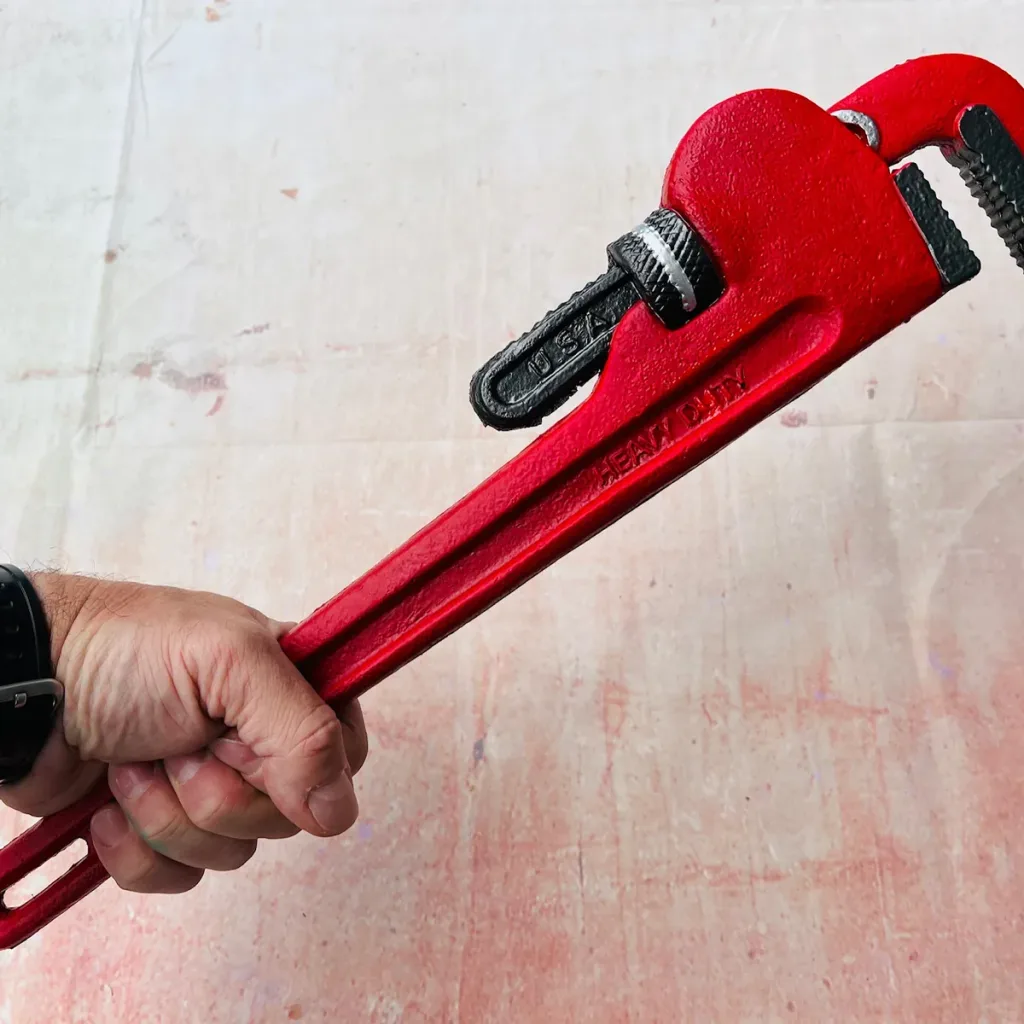 Hand gripping red safe PU foam pipe wrench marked USA, shown diagonally against a pale textured background.