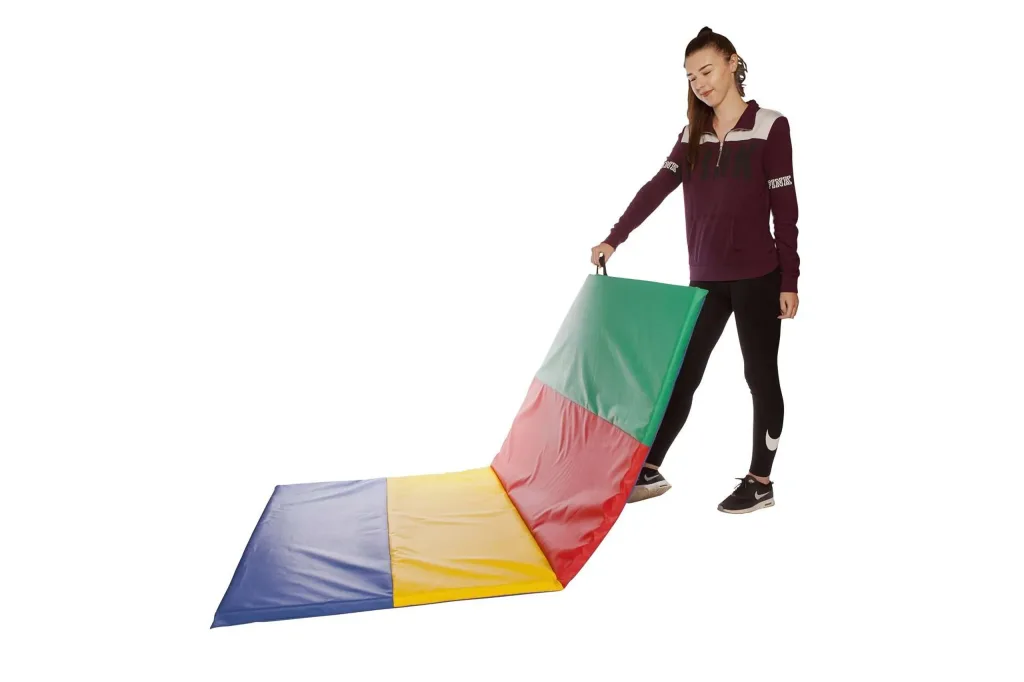 Person holding a carry-handle of a partially unfolded giant folding tumble mat with green, red, yellow, and blue panels.