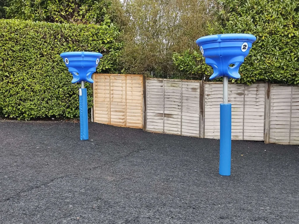 Two blue round post pads on metal poles supporting blue funnel-shaped play baskets marked 2 on a black rubber play surface.