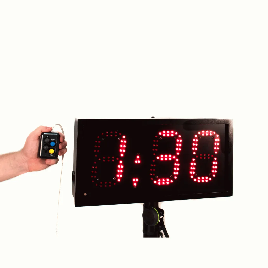 LED lap counter with red 3-digit display reading 9:38 on a tripod, with a hand holding the wired remote control.