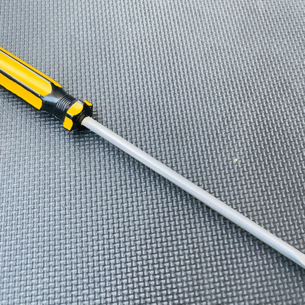 Yellow-and-black handled PU foam training screwdriver with gray shaft lying diagonally on a textured gray mat.