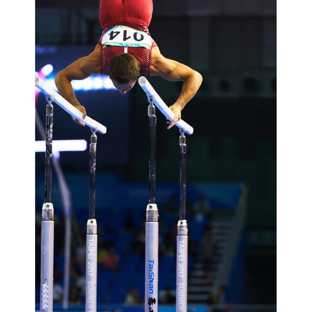 Gymnast in a red singlet upside down on parallel bars, gripping white bars above metal posts, bib reads 014.