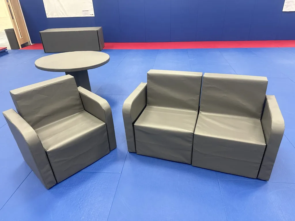 Gray foam three-seat sofa and matching armchair with heavy-duty PVC covers and armrests arranged on blue training mats beside a round table.