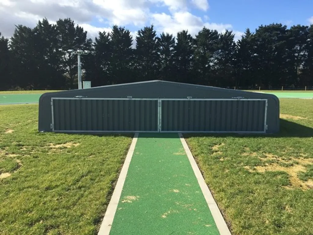 Galvanised steel pole vault wheel away cover with two corrugated panels closed over a green runway.