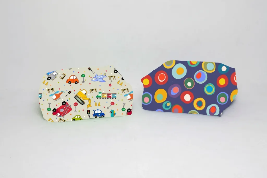 Two padded child bean bags on a white floor, one cream with vehicle and construction prints and one dark blue with multicolored circles.