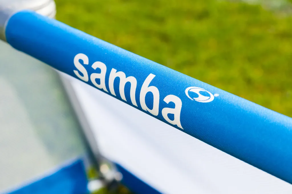 Blue aluminium goal bar with the text samba, white netting beneath and blurred green grass in the background.