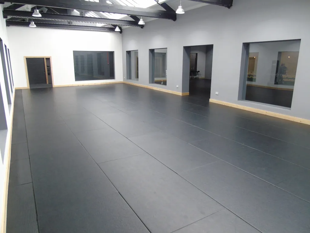 Large open training room with black training mats covering the floor and a door labeled MALE on the far wall.