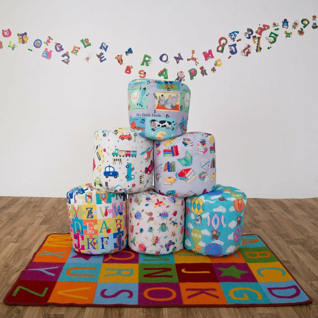 Set of six educational child bean sitting pods with printed nursery scenes (including text 'Hey Diddle Diddle'), stacked on a colorful alphabet rug.