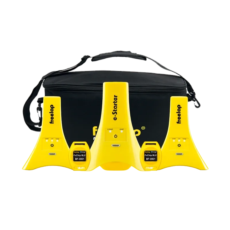 Three yellow timing devices—center labeled e-Starter and sides labeled freelap—with two small modules reading FxChip BLE BF-0001, set before a black satchel bag.